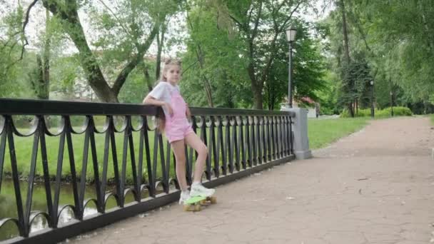 Ung vacker söt flicka med långt hår står på en skateboard nära staketet. — Stockvideo
