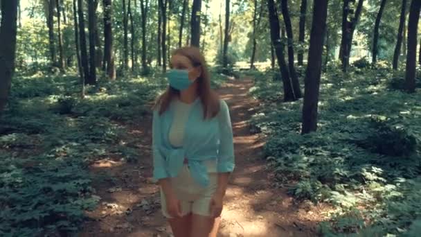 La donna con una maschera medica sta camminando lungo la strada intorno alla foresta. 4k — Video Stock
