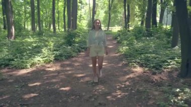 Güzel genç kız yazın parkta yürür. Güneşli aydınlık bir gün. 4k