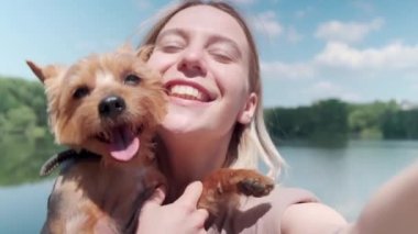 Kız köpeğini elinde tutuyor ve gölün arka planında fotoğraf çekiyor..