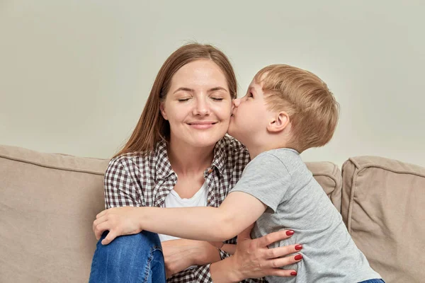 Mom and son together on the couch. Boy kisses his beloved mother on the cheek.