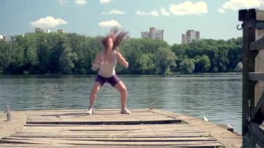 Kızın atletik bir vücudu var. Çömelme hareketleri. Gölde spor aktiviteleri.