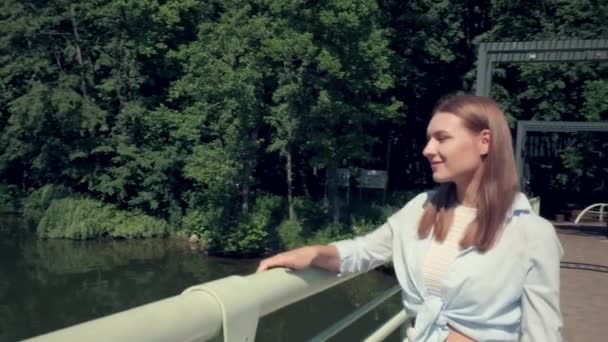 Hermosa chica camina a través del puente en un día caluroso de verano y disfruta de la vista. — Vídeos de Stock