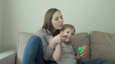 Çocuk sabun köpüğü yakalıyor. Anne ve oğlu evde oynayıp köpük üflüyorlar..