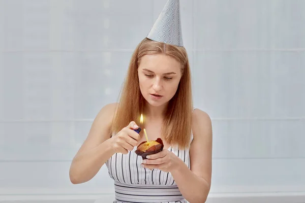 Красивая молодая девушка зажигает праздничный кекс на свой день рождения. — стоковое фото