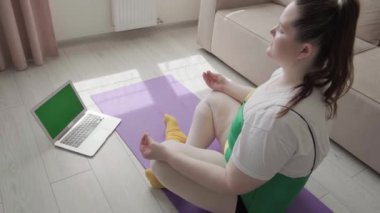 Şişman bir genç kız yoga yapıyor ve internetten video dersi izliyor..