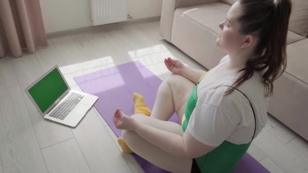 Ein übergewichtiges junges Mädchen praktiziert Yoga und schaut sich eine Videostunde online an. — Stockvideo