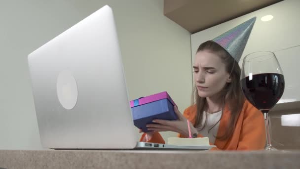 Woman opens a gift while sitting at a laptop. Birthday celebration online. — Stock Video