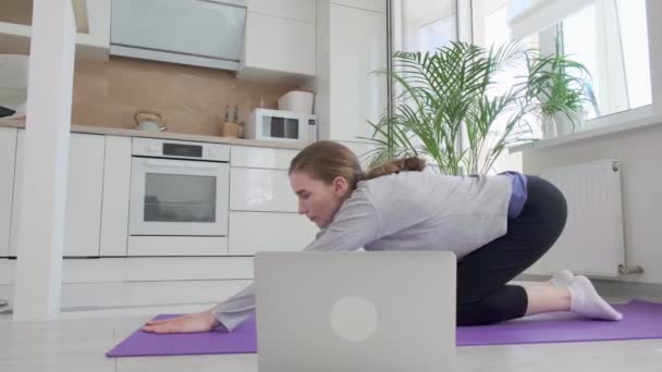 Eine athletische Frau in Sportbekleidung sitzt auf dem Boden, macht Yoga auf einer Matte. — Stockvideo
