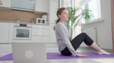 Bir spor kadını dizüstü bilgisayarından eğitim dersini açar ve spor yapmaya başlar..
