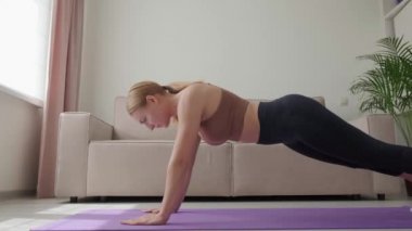 Atletik vücutlu genç bir kadın kalas egzersizi yapıyor. Evde spor yapıyorum..