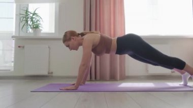 Atletik vücutlu genç bir kadın kalas egzersizi yapıyor. Evde spor yapıyorum..