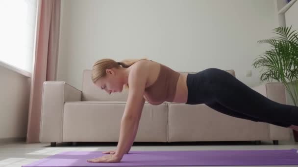 Mujer joven con cuerpo atlético haciendo ejercicio de tablón. Hacer deporte en casa. — Vídeo de stock