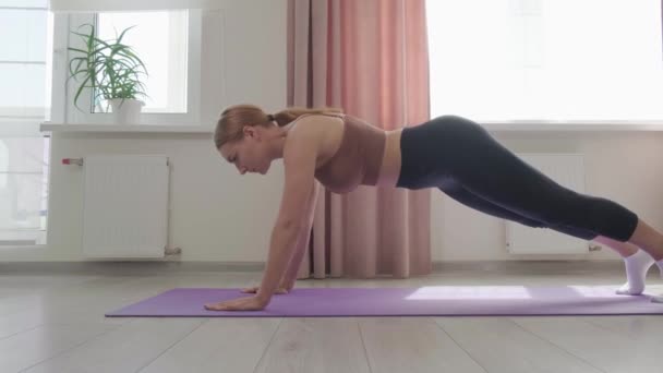 Mujer joven con cuerpo atlético haciendo ejercicio de tablón. Hacer deporte en casa. — Vídeo de stock