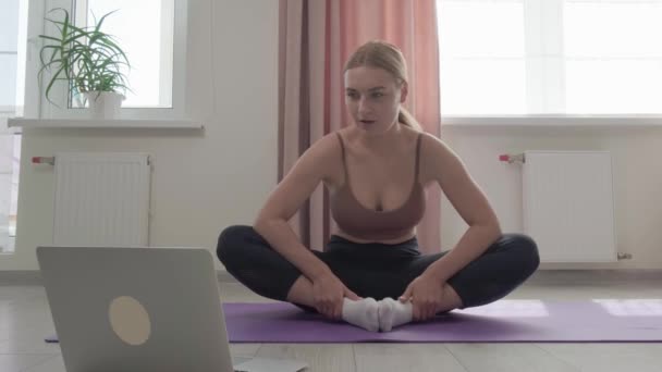 The sporty woman in a top is engaged in yoga and looks at the laptop screen. — Stock Video