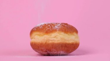 Doldurulmuş yuvarlak çörek. Yukarıdan pudra şekeri uçuyor. Pembe arkaplan.