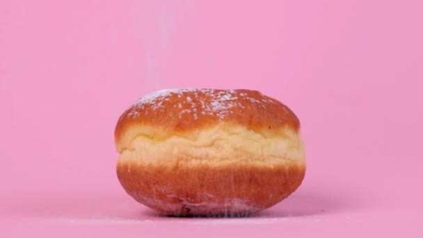 Bonito donut redondo con relleno. El azúcar en polvo vuela desde arriba. Fondo rosa. — Vídeos de Stock