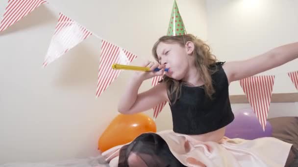 Une fille en vêtements lumineux et une casquette festive danse et regarde la caméra. — Video