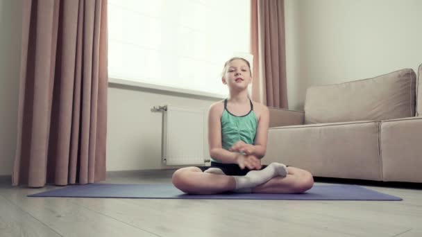 Das Mädchen sitzt in der Lotusposition auf dem Teppich im Wohnzimmer. — Stockvideo