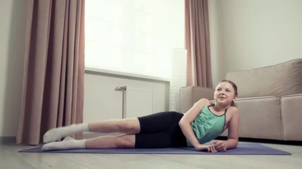 Het meisje gaat sporten en tilt haar been op. Sport thuis. Atletisch lichaam — Stockvideo