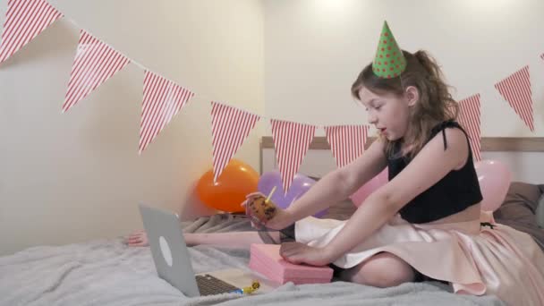 Pige fejrer sin fødselsdag online, holder en cupcake med et lys. – Stock-video