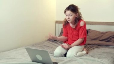 Sevimli bir kız yatağında dizüstü bilgisayarının önünde video bağlantısı kullanarak yatıyor..