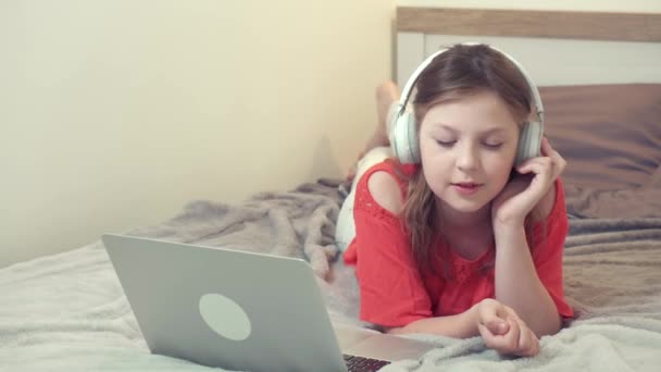 Menina bonita deitada na cama ouvindo música com fones de ouvido brancos. — Vídeo de Stock