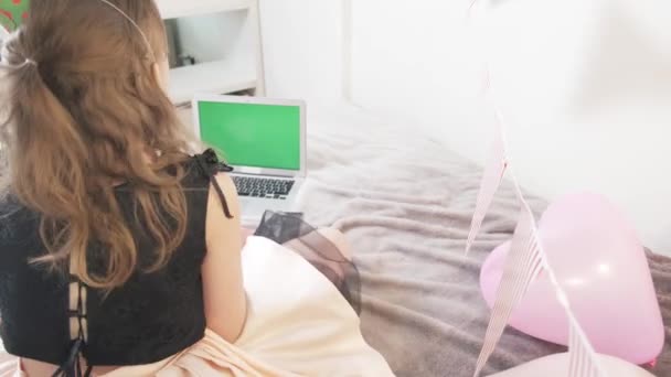 La fille d'anniversaire s'assoit avec son dos et regarde dans le moniteur d'ordinateur portable vert. — Video