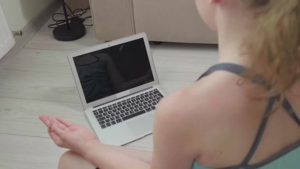 Dívka sedí se zády na obrazovce notebooku a dělá jógu.