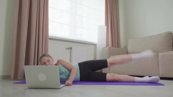 La chica va a hacer deporte en casa y levanta la pierna. Hacer deportes en casa. — Vídeos de Stock