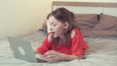 Esmer bir kız beyaz bir yatakta uzanıyor ve internetten iletişim kuruyor..