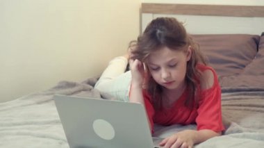 Yatağa uzanmış ev ödevini düşünen bir kız. Önünde bir laptop var..