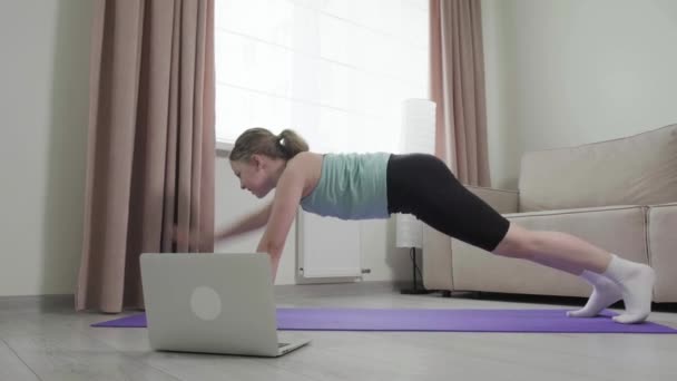 Hacer ejercicios de tablón de pérdida de peso y mirar un monitor portátil. Formación en línea. — Vídeos de Stock