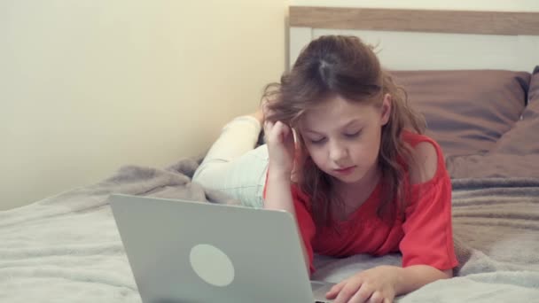 Uma rapariga deitada na cama a pensar nos trabalhos de casa. Na frente dela está um laptop. — Vídeo de Stock