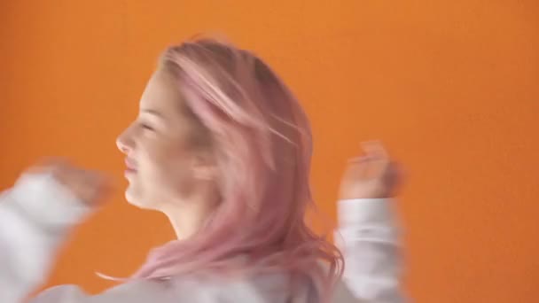 En ung vacker kvinna snurrar på ett ställe och ler. Orange bakgrund. — Stockvideo