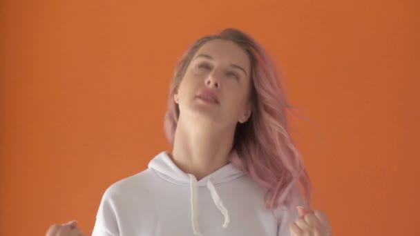 Rapariga frustrada com cabelo rosa olha para a moldura. Fundo laranja. — Vídeo de Stock