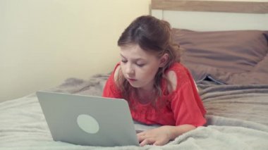 Yatağa uzanmış ev ödevini düşünen bir kız. Önünde bir laptop var..