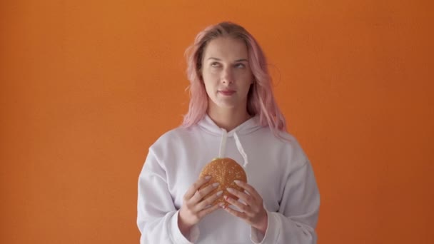 Uma mulher segura um hambúrguer em suas mãos, ela está em uma dieta, fast food é proibido. — Vídeo de Stock