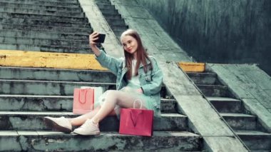 Merdivenlerde oturan güzel genç kız telefonda selfie çekiyor..