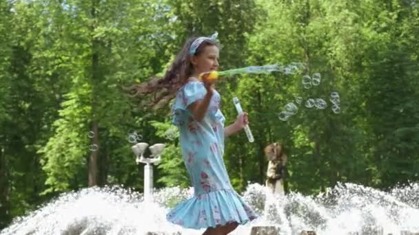 Een mooi meisje draait en blaast bellen in het park in de zomer. — Stockvideo
