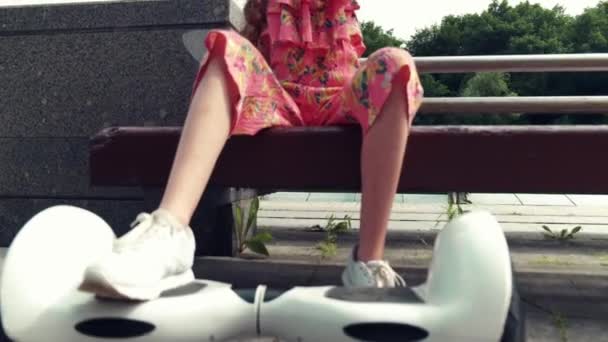 Ένα όμορφο κορίτσι κάθεται στο πάρκο σε ένα παγκάκι και βγάζει μια σέλφι.. — Αρχείο Βίντεο
