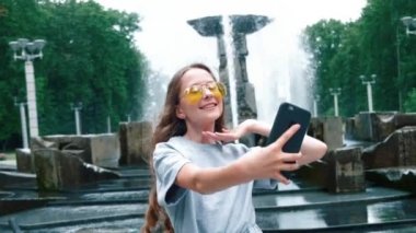 Dalgalı saçları ve şık gözlükleriyle güzel mutlu bir kız selfie çekiyor..