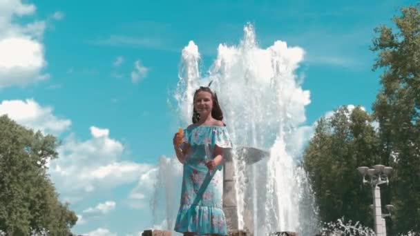 Una hermosa chica en un vestido de cuerpo entero cerca de la fuente sopla burbujas. — Vídeo de stock