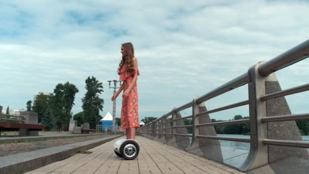 Movimiento lento de una chica montando un scooter giratorio. En el fondo del río — Vídeos de Stock