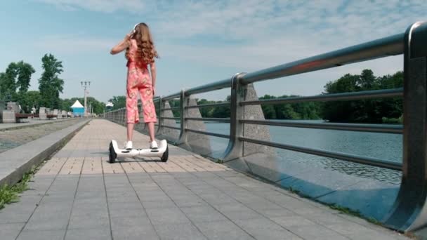 Een uitzicht van de achterkant van een meisje rijden een hoverboard en het luisteren naar muziek. — Stockvideo