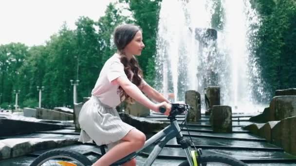 En tjej med långt vågigt hår cyklar i slow motion. Sommarpark. — Stockvideo