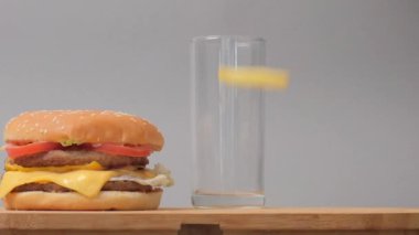 Masada bir hamburger ve boş bir bardak var. Kızartmalar düşüyor, uçuyor.