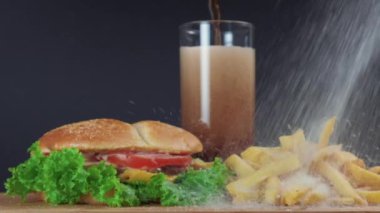 Bir sandviç ve patates, bir bardak soda, sağda beyaz tuz uçuşuyor..
