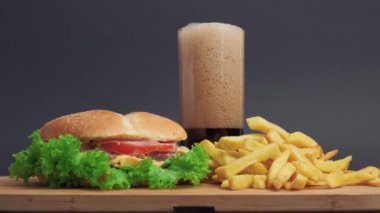 Tahta masada sandviç ve patates kızartması var. Yanında bir bardak soda var..