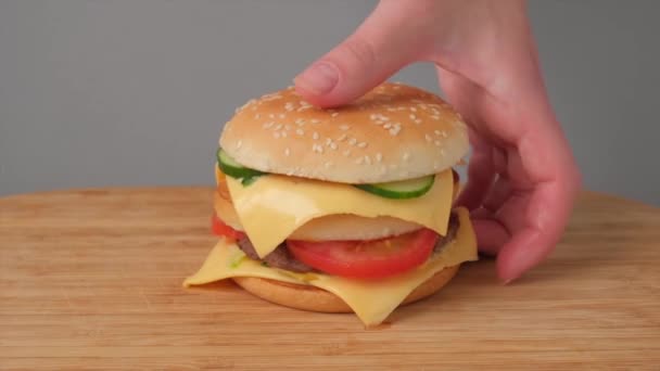 Una mano recoge una gran hamburguesa doble de queso jugosa de la mesa. — Vídeos de Stock